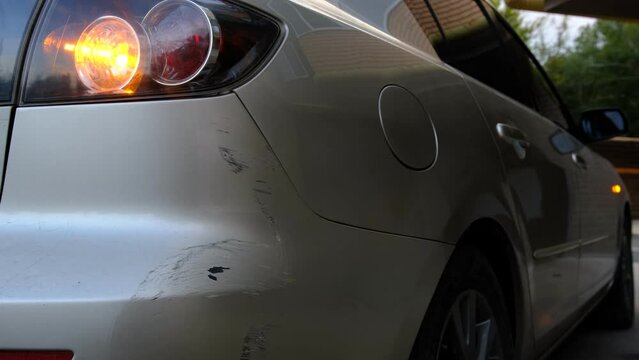 Scratch abrasion on car back bumper due to minor accident with flashing emergency yellow lights.