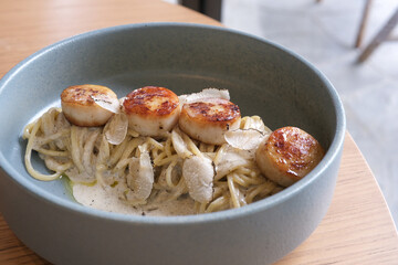 fettuccine spaghetti with scallop truffle cream sauce. Traditional authentic Italian pasta with Truffle Cream sauce and Grilled large Scallops with grill mark in blue round dish on fine dining table