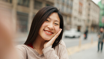 Fototapeta premium Cute Asian girl shooting video for social media looking happy outdoors. Young woman exploring new city having video call with friends