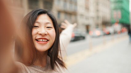 Asian female blogger smiling while taking self portrait on the street. Happy woman making content for her blog in city