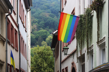 Fototapeta na wymiar Rainbow Flag hanging on the wall on the street in the center of Heidelberg, Germany. Buildings and cloudy sky on the background