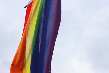 Fragment of the rainbow flag, a symbol for the LGBT community, hanging waving in the wind with a cloudy sky background