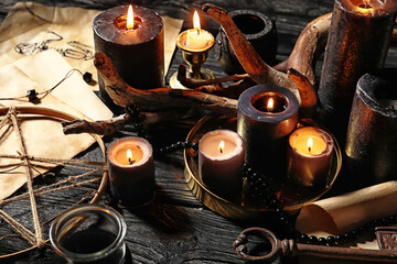 Burning candles and magic attributes for ritual on dark wooden wizard table