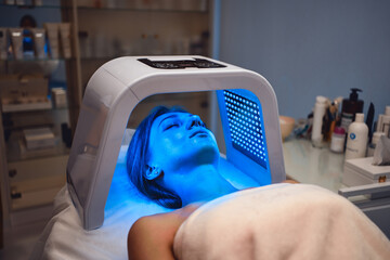 A young woman takes care of her skin with an LED mask in a beauty salon.