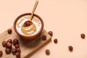 Wooden board with bowl of delicious hazelnut butter on color background