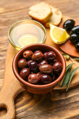 Board with bowls of delicious olives and oil on wooden table, closeup
