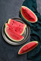 Plate with slices of watermelon and napkin on dark background