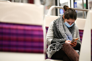 A person wearing a surgical mask and checking her phone on public transport due to a pandemic...