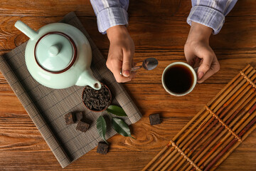 Female hands with cup of puer tea and dry pressed leaves on wooden background
