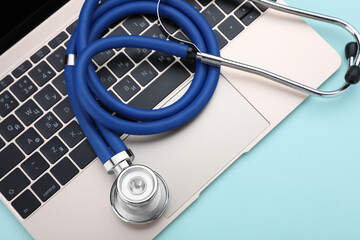 Laptop and stethoscope on turquoise background, closeup