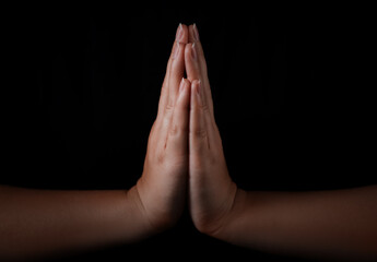 Woman holding hands clasped while praying against black background, closeup