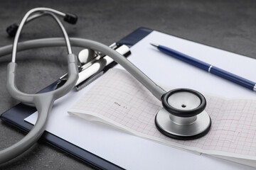 Clipboard with stethoscope and cardiogram on grey table, closeup