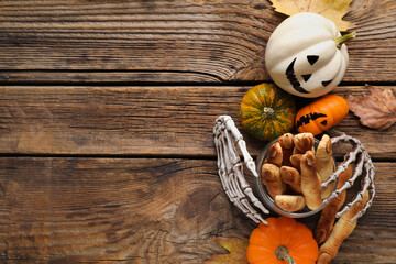 Halloween cookies, skeleton hands, fallen leaves and pumpkins on wooden background