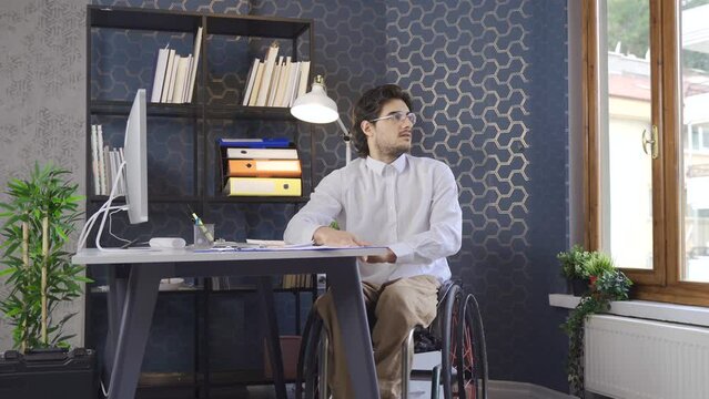 Disabled person in wheelchair works in office at computer.
Sad and tired disabled man about workflow.
