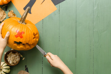 Woman carving Jack-O-Lantern pumpkin on green wooden background