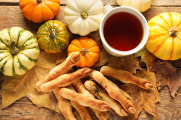 Witch finger cookies with cup of tea, pumpkins and fallen leaves on wooden background