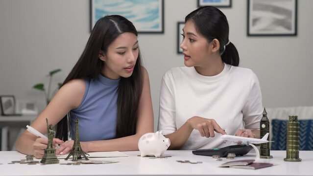 Young Asian lesbian couple plans to save money for a trip around the world. Travel budget concept. passport, monument model and aircraft toy in the picture. Lgbt couple lifestyle.