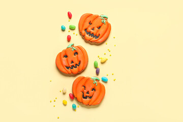 Tasty Halloween pumpkin cookies with jellies on beige background