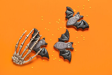 Tasty Halloween bat cookies and skeleton hand on orange background