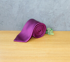 Rolled silk burgundy tie isolated on a wood background. Elegant accessory,  gentleman and necktie...