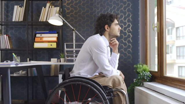 Disabled businessman in wheelchair looking out the window.
A worker sitting in a wheelchair looks out the window in the office and is thoughtful.

