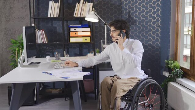 Office worker disabled businessman talks by phone and works with computer.
Disabled office worker sitting in a wheelchair and talking on the phone.
