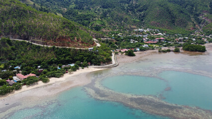 Beautiful white sandy beach coastline of Metiaut in capital Dili, Timor Leste, aerial drone view of ocean and green hill landscape during wet season on tropical island