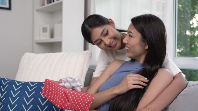 Asian lesbian woman congratulates her girlfriend on birthday, LGBT woman makes surprise, gives to beloved woman gift box with present, family celebrating life events, hugging expressing love.