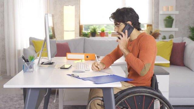 Self-employed disabled teenager sitting in his wheelchair and talking on the phone.
Disabled young man working with computer at home and talking on the phone.
