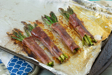 Baked asparagus bunches wrapped in prosciutto slice on aluminum foil lined baking sheet on hot pads