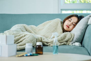 Obraz na płótnie Canvas Young Asian woman sick, tired, she sleep and resting on blue fabric sofa and blanket after takes medicines pills in living room at her home. Woman use the phamacy first aid kit box
