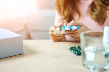 Young Asian woman sick, tired, she sitting and resting on blue fabric sofa and blanket after takes medicines pills in living room at her home. Woman use the phamacy first aid kit box.