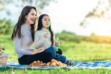 Happy asian family mom and her doughter in the garden, They are having fun playing and blowing bubbles.