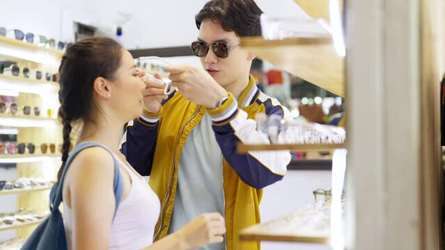 Young Asian couple enjoy and fun outdoor lifestyle shopping together at street market on summer holiday vacation. Happy man and woman choosing and buying fashion sunglasses together at street market.