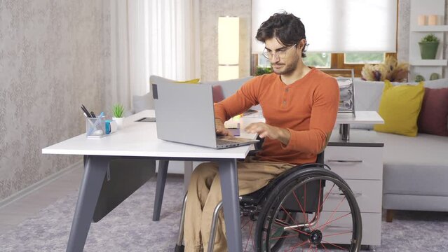Disabled teenager working with laptop sitting in wheelchair.
Disabled teenager sitting in a wheelchair works at his desk at home.
