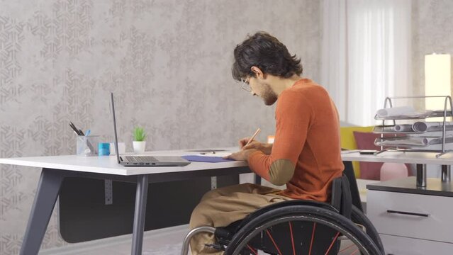 Joyful disabled businessman works at home with laptop and earns.
Disabled teenager sitting in a wheelchair works at his desk at home.
