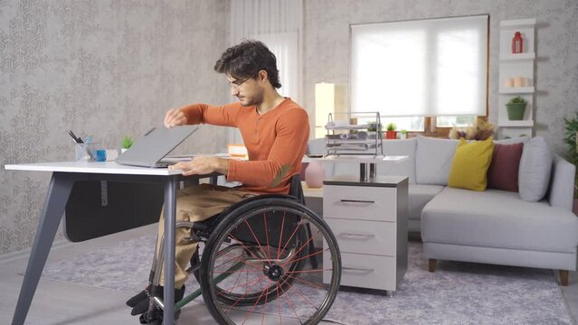 Disabled teenager in wheelchair working with laptop.
Disabled teenager sitting in a wheelchair works at his desk at home.
