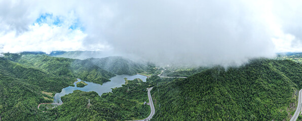Bird's-eye view of a mountain view overlooking the road and mist surrounding mountains, green forests and rivers.