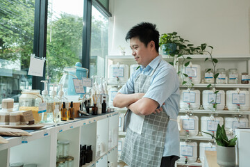 Portrait of happy Thai Asian male shopkeeper arms crossed and smiles at refill store, arrange...