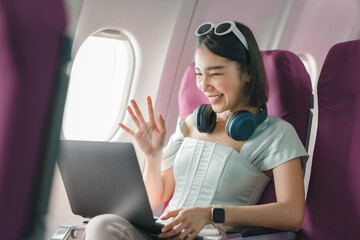 Fototapeta premium Joyful asian woman sits in the airplane and using laptop while go to travel