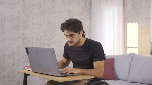 Disabled young man working hard with laptop.
Disabled teenager working at home focused on laptop.
