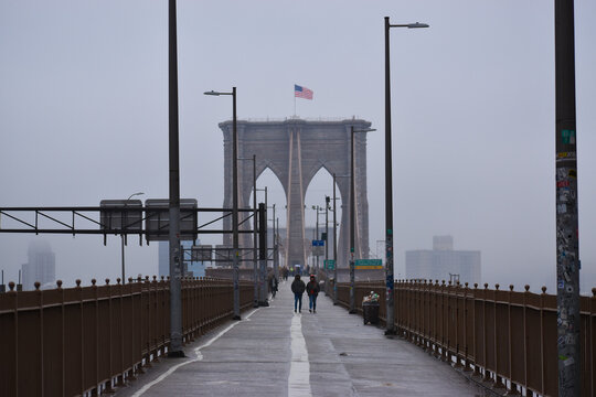 People are seen walking across Brooklyn Bridge in New York City on a foggy day, March 17, 2022.