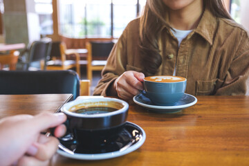 Closeup image of a couple holding and drinking coffee together in cafe