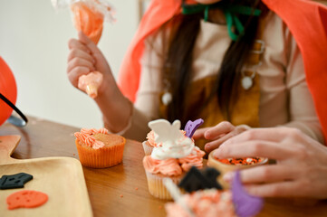 A cute young Asian girl enjoys making a Halloween cupcake with her mom. cropped shot