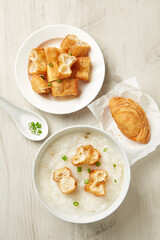 Top view of bowl of traditional Chinese porridge and fritters on woooden table.