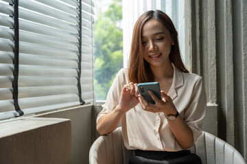 Young woman using smartphone at table with laptop in coffee shop