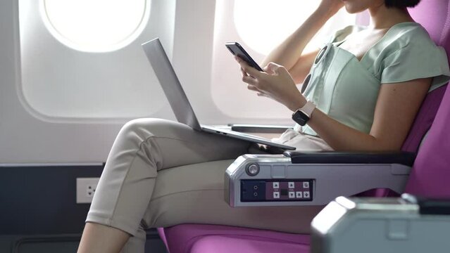Joyful asian woman sits in the airplane and using mobile phone while go to travel