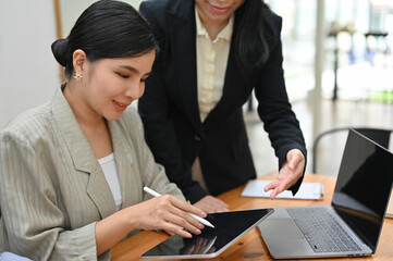 Asian female boss checking her meeting schedule on tablet with her assistant.