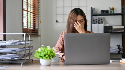 Stressed millennial Asian businesswoman suffering from headache or eyes strain.