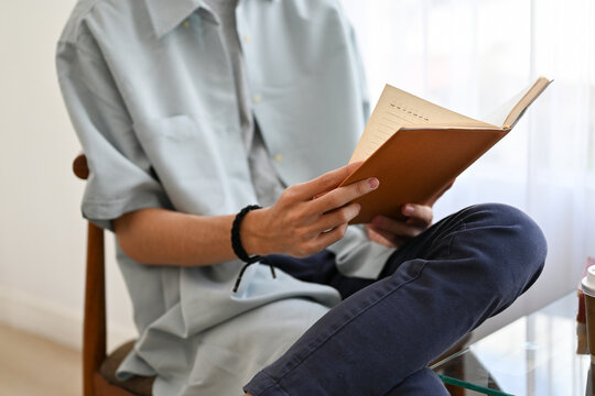 cropped image, A young Asian man reading a book while relaxing in the cafe.